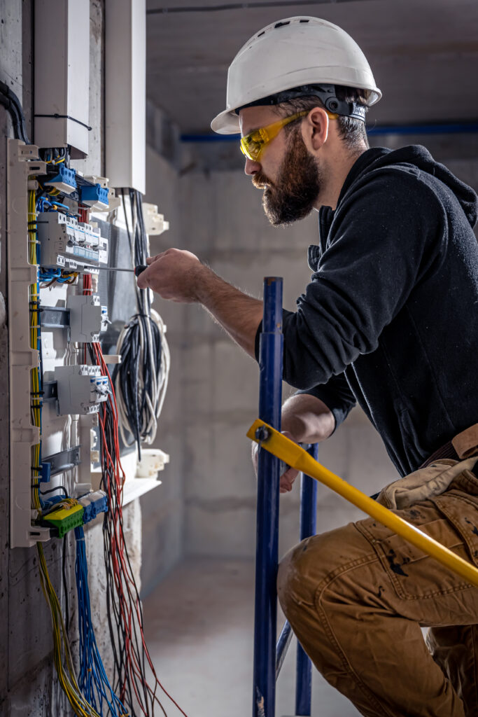 a male electrician works in a switchboard with an electrical connecting cable.